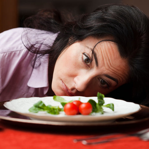 young woman looking sadly at plate of salad, diet concept