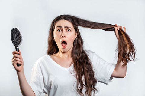 A frightened woman with long dark hair, screaming, holding a comb and a lock of her long hair.