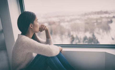 Young woman gazing out the window at winter landscape, winter blues concept, mental health in winter