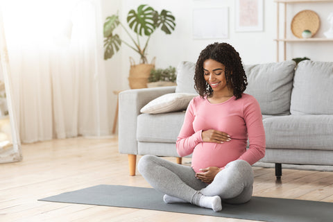 Beautiful happy pregnant african woman hugging her tummy, sitting on sport mat, enjoying her pregnancy